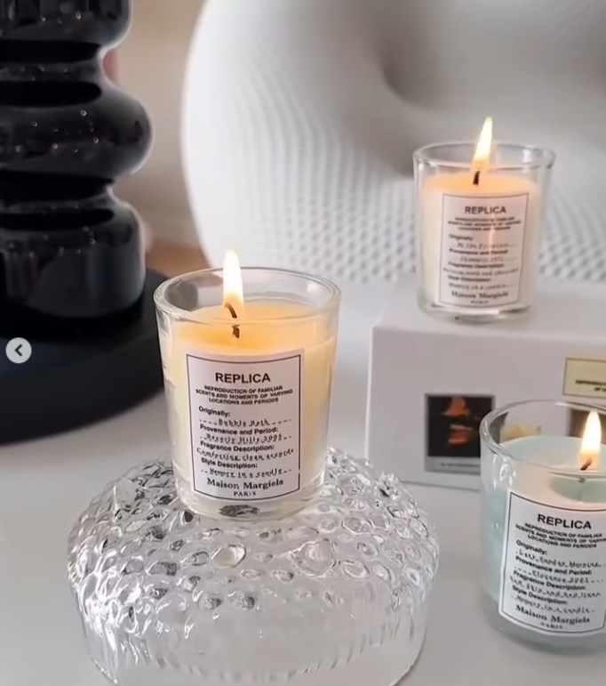 These are Maison Margiela Replica scented candles, featuring glass jars with minimalist white cotton labels reminiscent of their fragrance bottles. - Other Brand Candles | Aleppo Gift UAE
